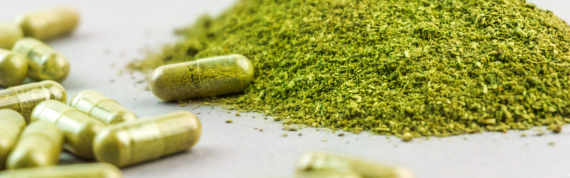 a pile of ground kratom next to capsules filled with the ground plant