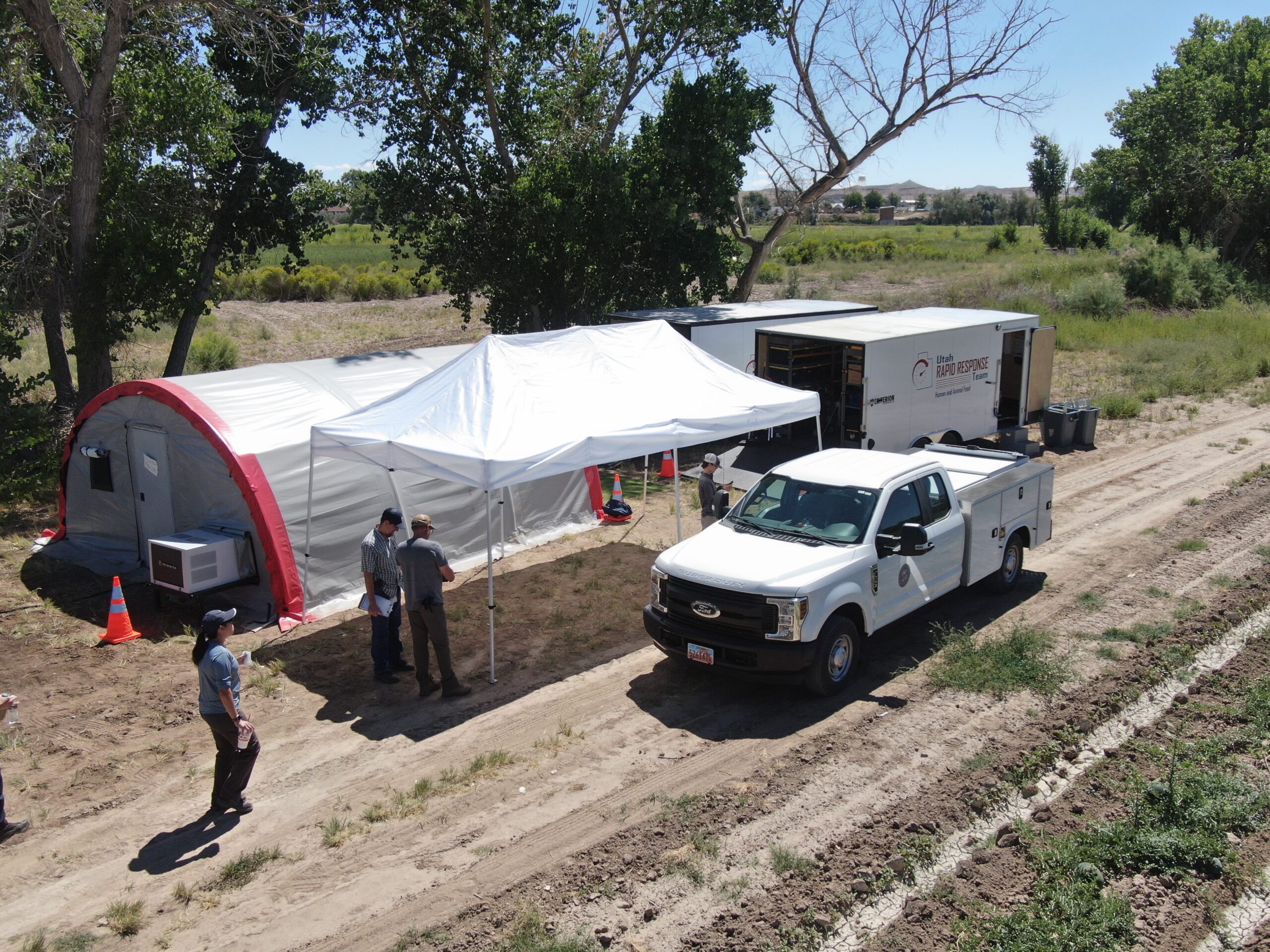 a white truck, tent, and trailer set up in a field to respond to an illness outbreak