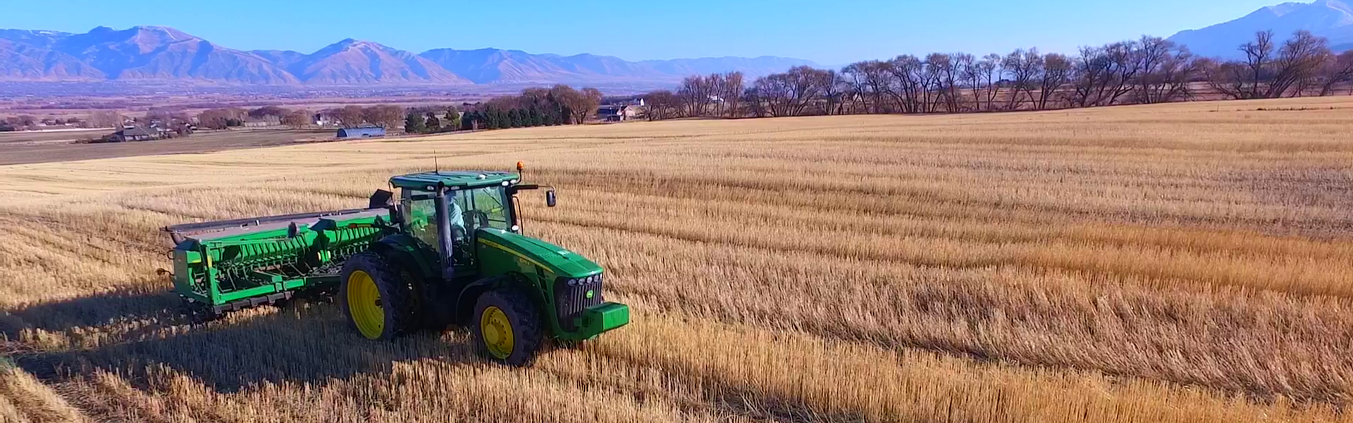 a tractor driving through a field with mountains and blue sky in the background