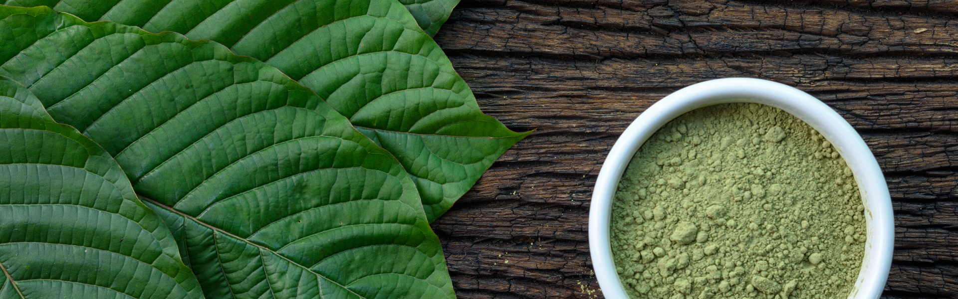 kratom leaves and a green powder sitting on a wooden table
