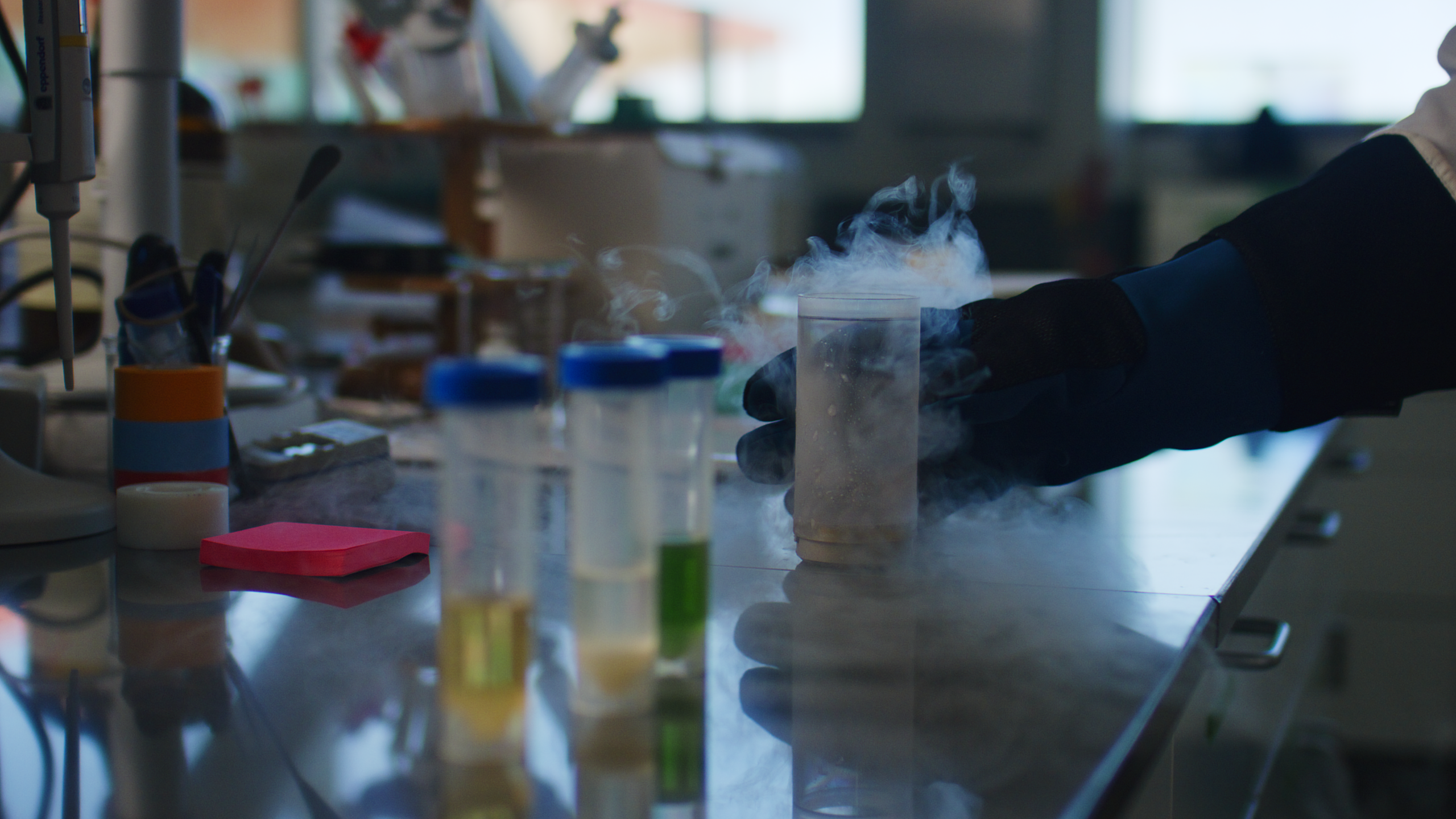 a lab tech with an insulated glove holds a steaming beaker