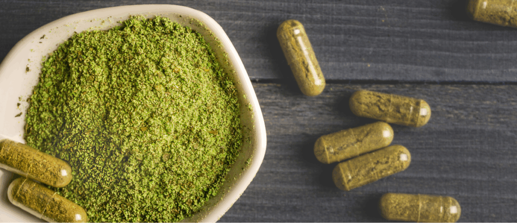 kratom capsules and a green powder sitting on a wooden table