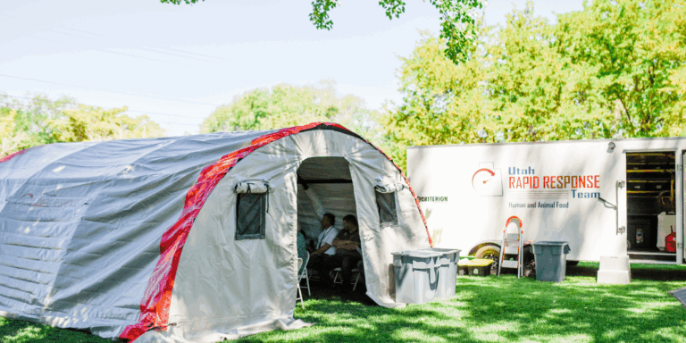 a white tent with an orange border sitting on a green lawn in front of a trailer that reads Utah Rapid Response Team