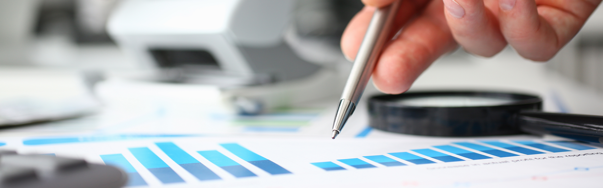 a hand holding a metal pen pointing to a paper listing nondescript graphs